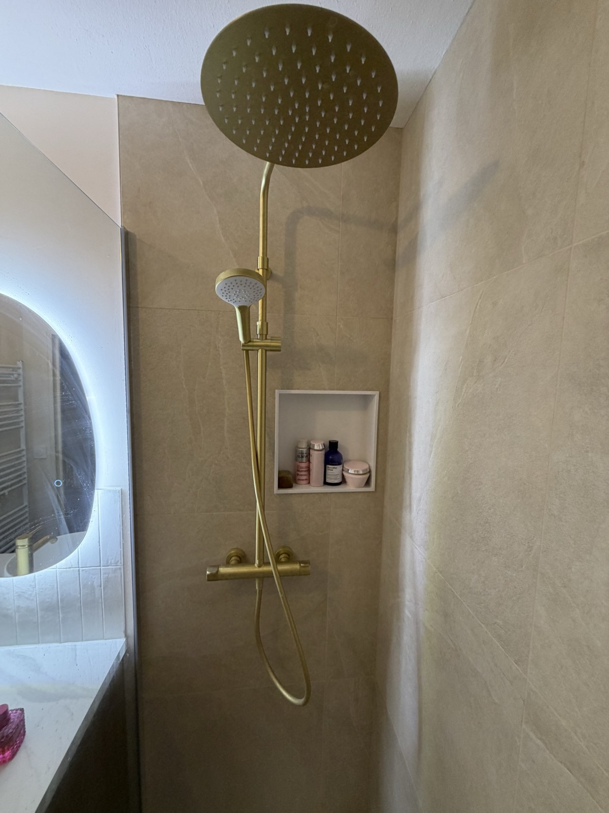 Douche à l'italienne carrelée grand format, niche de rangement et robinetterie dorée